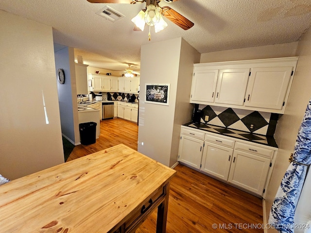 kitchen with backsplash, stainless steel dishwasher, a textured ceiling, hardwood / wood-style flooring, and white cabinets