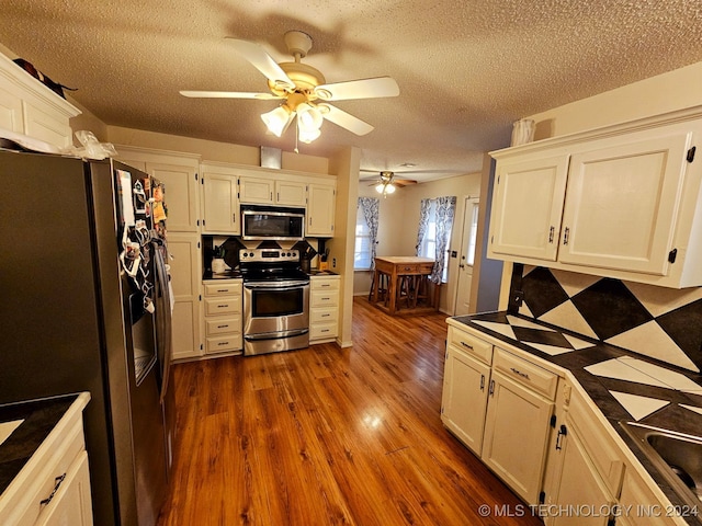 kitchen with white cabinets, appliances with stainless steel finishes, a textured ceiling, and dark wood-type flooring