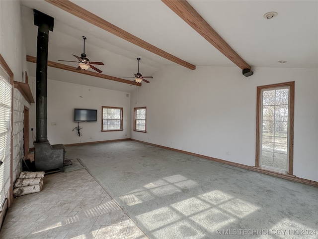 unfurnished living room with vaulted ceiling with beams, a wood stove, plenty of natural light, and ceiling fan