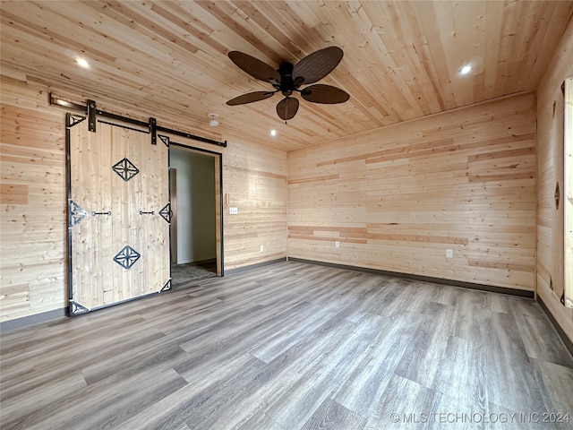 unfurnished room featuring a barn door, wood walls, wooden ceiling, and hardwood / wood-style flooring