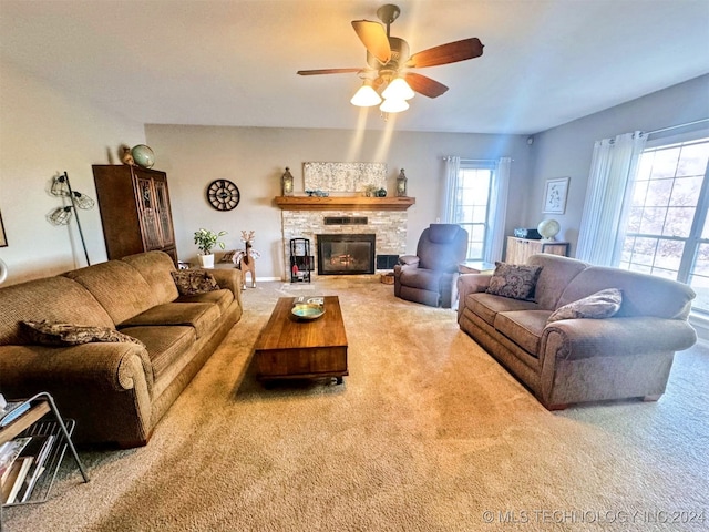 carpeted living room with a stone fireplace and ceiling fan