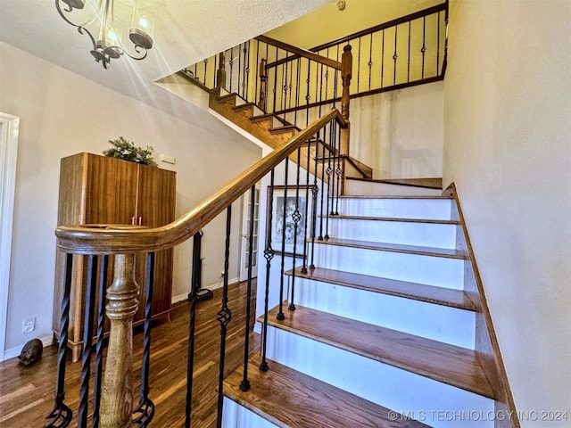 staircase with wood-type flooring and an inviting chandelier