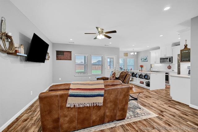 living room featuring light hardwood / wood-style flooring, ceiling fan with notable chandelier, and sink