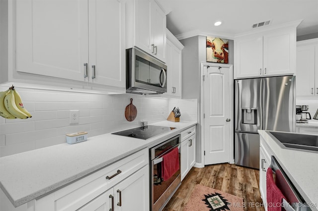 kitchen featuring white cabinets, crown molding, light wood-type flooring, appliances with stainless steel finishes, and tasteful backsplash