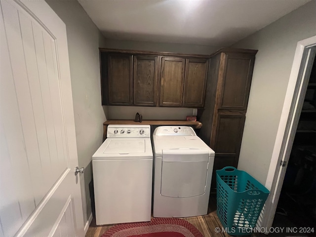 laundry area featuring washing machine and clothes dryer, cabinets, and wood-type flooring