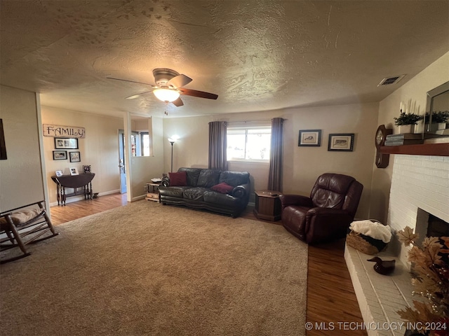 living room with wood-type flooring, a textured ceiling, a brick fireplace, and ceiling fan