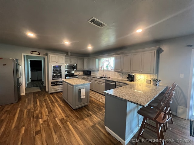 kitchen with a center island, a kitchen breakfast bar, dark hardwood / wood-style flooring, kitchen peninsula, and appliances with stainless steel finishes