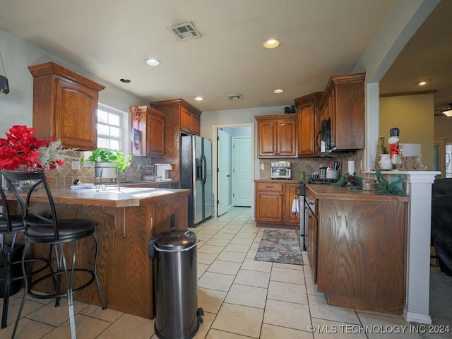 kitchen with backsplash, a kitchen breakfast bar, light tile patterned floors, kitchen peninsula, and stainless steel appliances