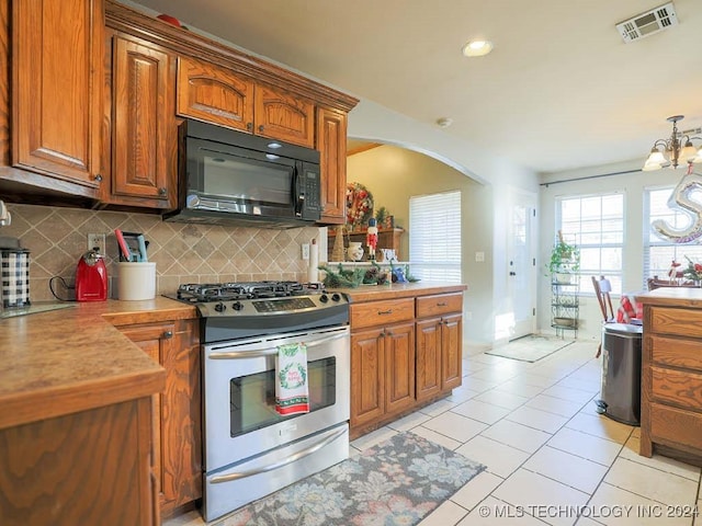 kitchen featuring decorative backsplash, gas range, a notable chandelier, and light tile patterned flooring