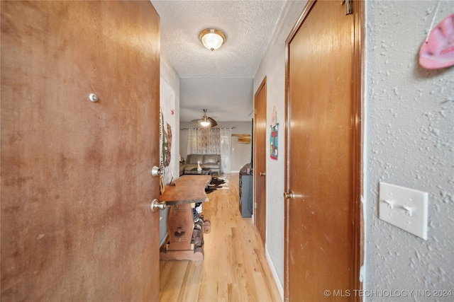 hall with a textured ceiling and light wood-type flooring