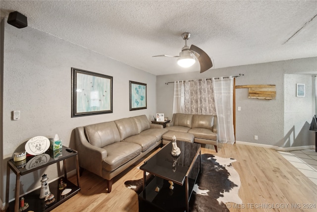 living room featuring ceiling fan, light hardwood / wood-style flooring, and a textured ceiling