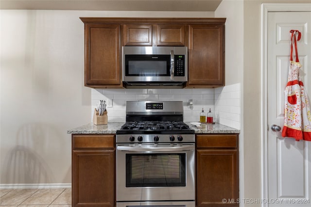 kitchen featuring backsplash, light stone counters, light tile patterned floors, and stainless steel appliances