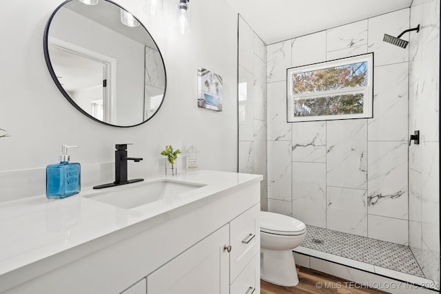 bathroom featuring toilet, wood-type flooring, vanity, and a tile shower