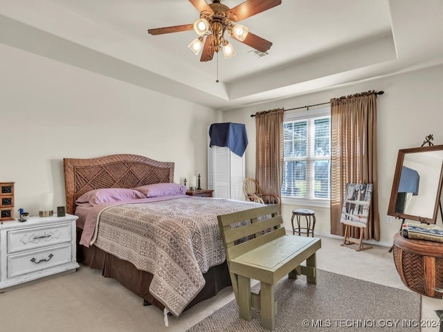 carpeted bedroom with a tray ceiling and ceiling fan