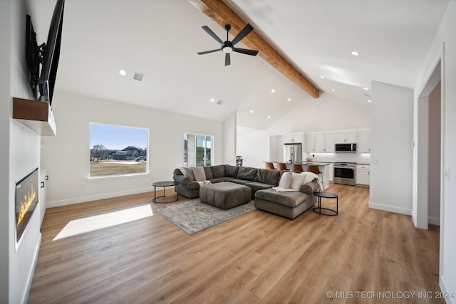 living room with beam ceiling, ceiling fan, a large fireplace, and light wood-type flooring