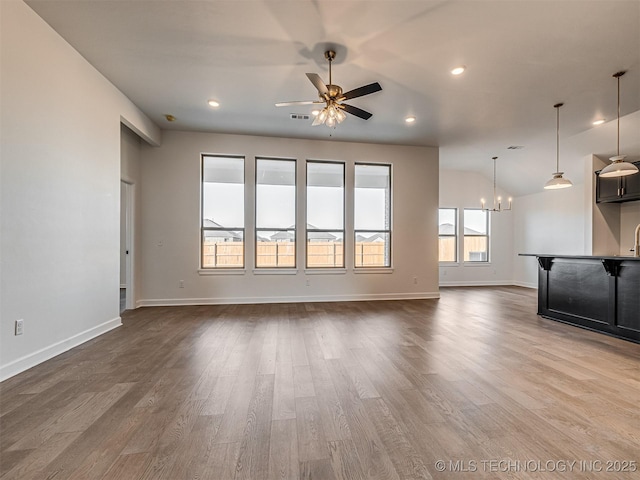 unfurnished living room featuring lofted ceiling, hardwood / wood-style floors, and ceiling fan with notable chandelier