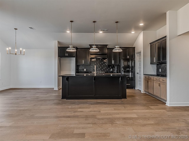 kitchen with tasteful backsplash, a center island with sink, light hardwood / wood-style flooring, pendant lighting, and black appliances