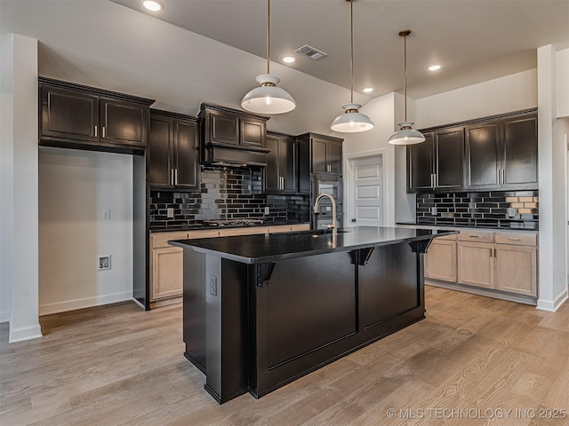 kitchen with hanging light fixtures, sink, a center island with sink, and light hardwood / wood-style flooring