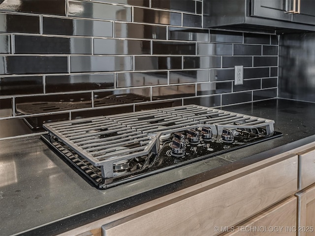 room details with black gas stovetop, backsplash, and dark stone counters