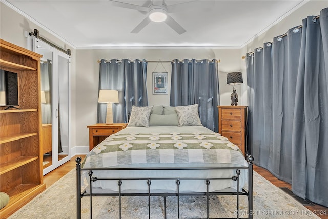 bedroom featuring a barn door, hardwood / wood-style flooring, ceiling fan, and crown molding