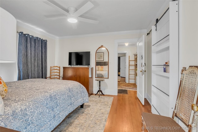 bedroom featuring a barn door, ceiling fan, light hardwood / wood-style flooring, and crown molding