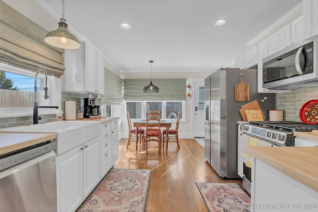 kitchen with decorative light fixtures, light hardwood / wood-style floors, white cabinetry, and appliances with stainless steel finishes