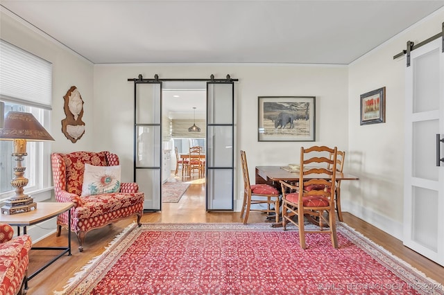 living area featuring a healthy amount of sunlight, a barn door, light hardwood / wood-style floors, and crown molding