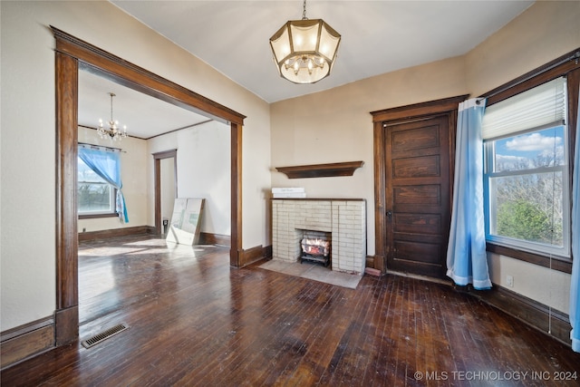 unfurnished living room featuring baseboards, visible vents, an inviting chandelier, wood-type flooring, and a brick fireplace