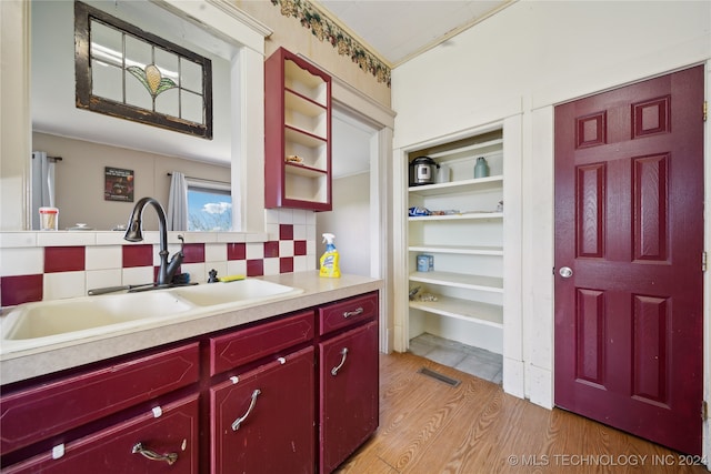 kitchen featuring decorative backsplash, light countertops, red cabinetry, and a sink