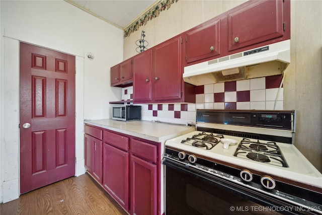 kitchen featuring under cabinet range hood, stainless steel microwave, wood finished floors, range with gas cooktop, and light countertops