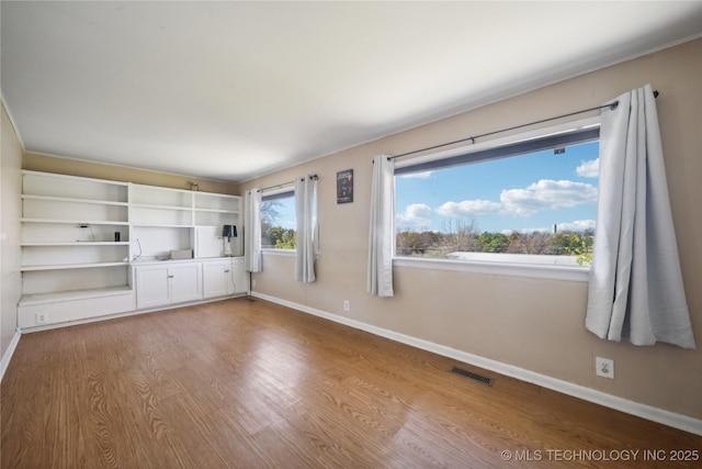 unfurnished living room featuring visible vents, baseboards, and wood finished floors