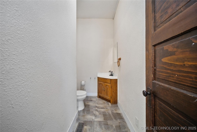 bathroom with visible vents, baseboards, toilet, a textured wall, and vanity