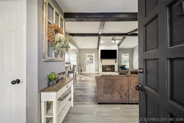 living room with ceiling fan, a fireplace, beamed ceiling, and light hardwood / wood-style floors