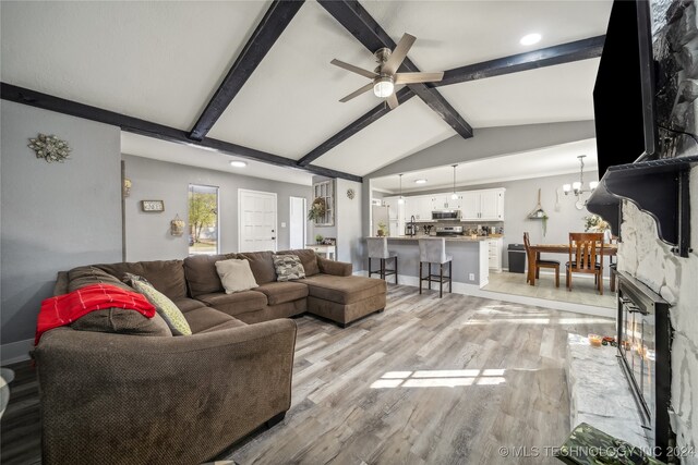 living room featuring a fireplace, lofted ceiling with beams, ceiling fan with notable chandelier, and light wood-type flooring