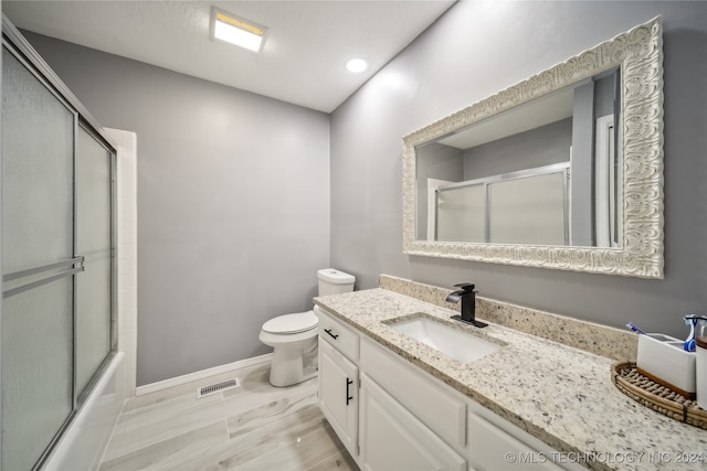 full bathroom featuring shower / bath combination with glass door, vanity, wood-type flooring, and toilet