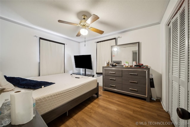 bedroom with dark hardwood / wood-style floors, ceiling fan, crown molding, and a closet