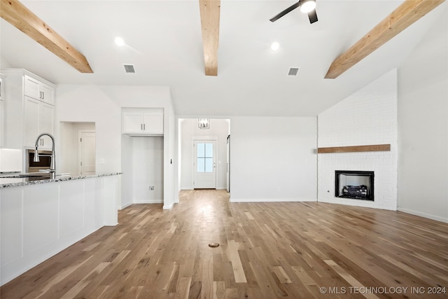 unfurnished living room featuring lofted ceiling with beams, sink, light hardwood / wood-style flooring, ceiling fan, and a fireplace