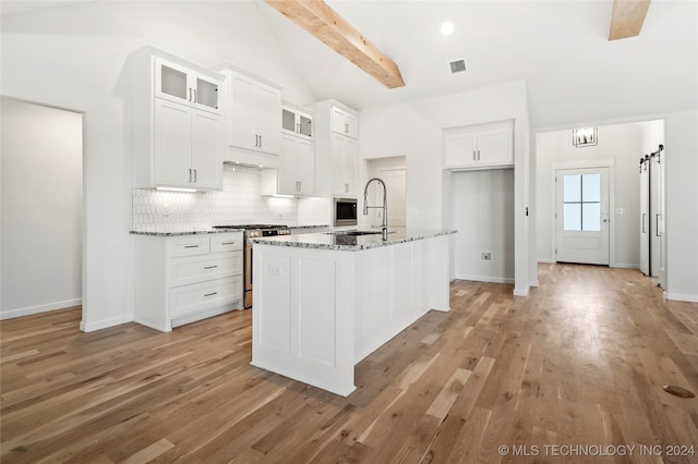 kitchen featuring stone counters, light hardwood / wood-style flooring, a barn door, an island with sink, and stainless steel appliances