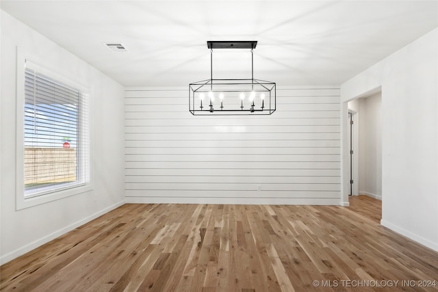 unfurnished dining area featuring hardwood / wood-style flooring, wooden walls, and an inviting chandelier