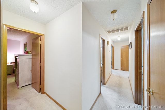 corridor with light carpet and a textured ceiling