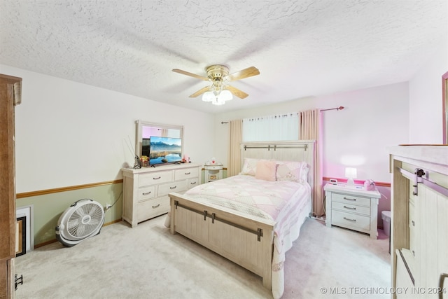 bedroom with ceiling fan, light colored carpet, and a textured ceiling