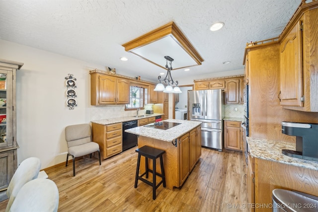 kitchen featuring a kitchen island, black appliances, decorative light fixtures, and light hardwood / wood-style floors