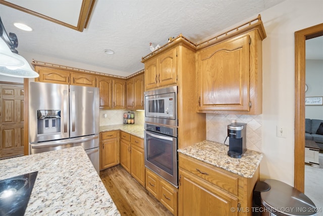 kitchen with appliances with stainless steel finishes, backsplash, light stone counters, decorative light fixtures, and light hardwood / wood-style floors