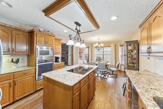 kitchen with light wood-type flooring, a textured ceiling, decorative light fixtures, a kitchen island, and stainless steel appliances