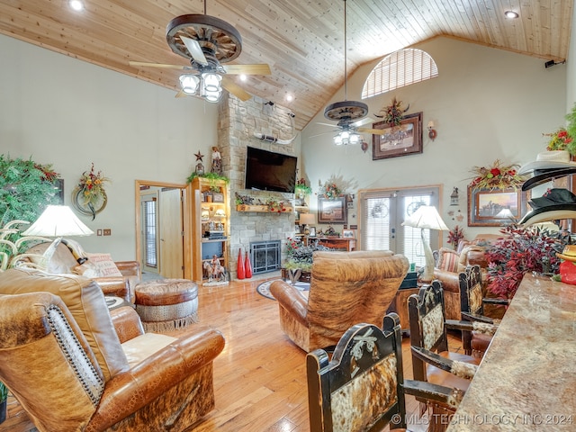 living room featuring light wood-type flooring, ceiling fan, high vaulted ceiling, wooden ceiling, and a stone fireplace