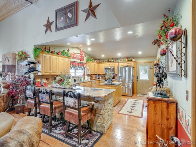 kitchen featuring a center island, vaulted ceiling, a breakfast bar area, appliances with stainless steel finishes, and light wood-type flooring