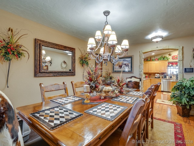 dining area with light hardwood / wood-style floors, a textured ceiling, and an inviting chandelier