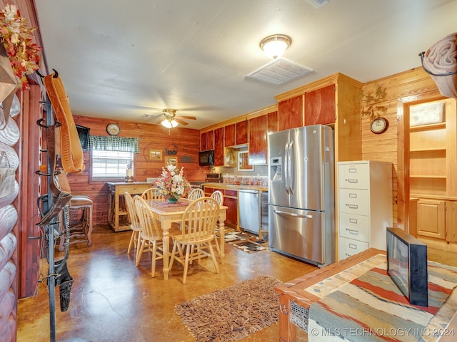 kitchen featuring ceiling fan, wooden walls, stainless steel appliances, and a textured ceiling