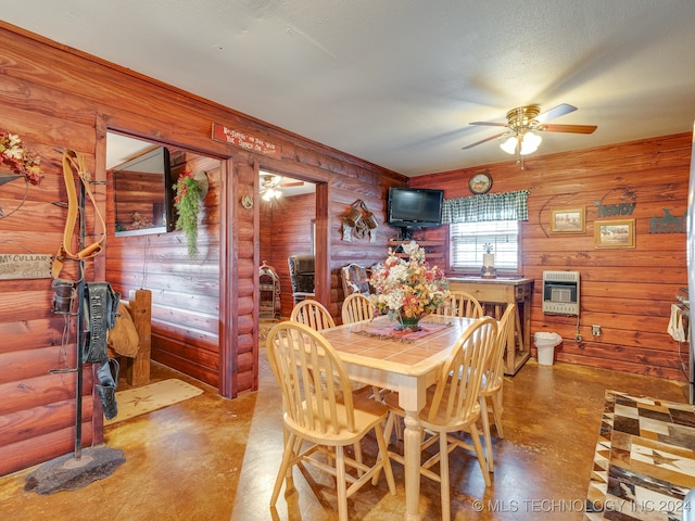 dining space with heating unit, ceiling fan, concrete flooring, and wood walls