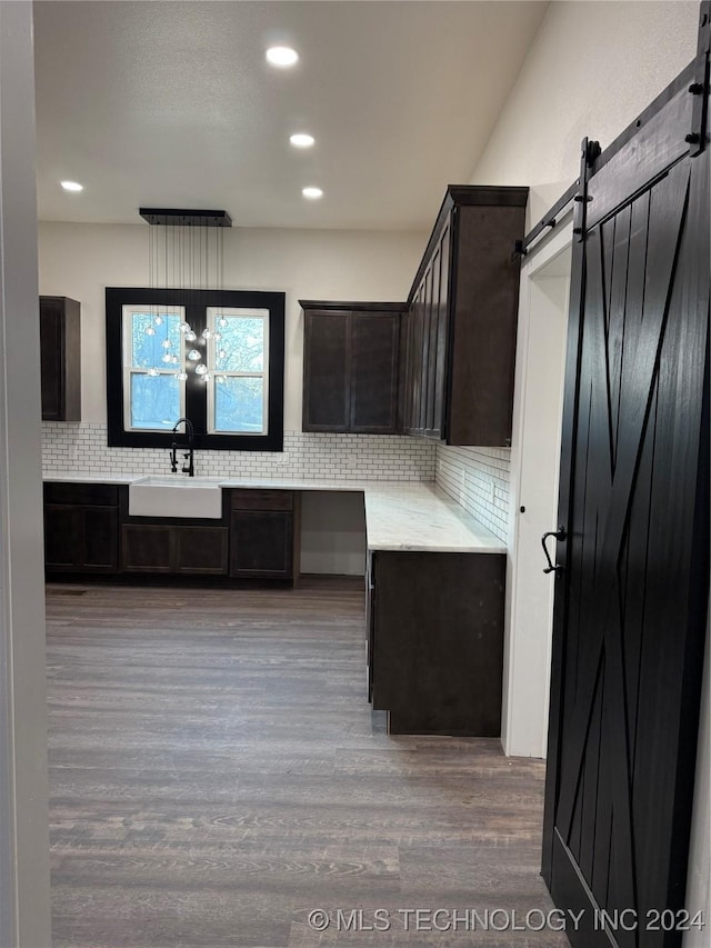 kitchen featuring dark brown cabinetry, sink, a barn door, backsplash, and wood-type flooring